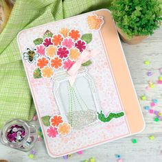 a card with flowers in a mason jar on top of confetti sprinkles