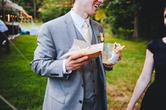 a man in a suit and tie holding a hot dog next to a woman wearing a black dress