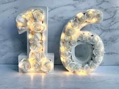 the number six is decorated with white roses and lit up by fairy lights in front of a marble background