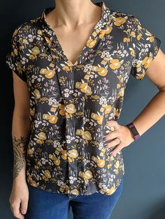 a woman standing in front of a blue wall wearing a black and yellow floral shirt