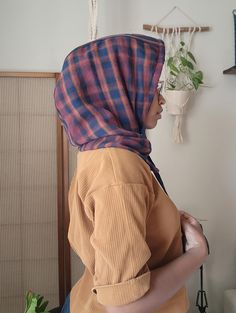 a woman wearing a plaid head scarf in front of a wall with plants on it