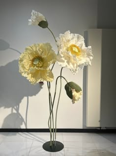 three white flowers are in a vase on the floor