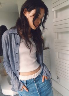 a woman standing in front of a white wall wearing blue jeans and a crop top