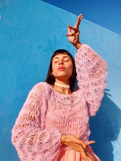 a woman standing in front of a blue wall with her hand up to the sky