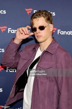 a man wearing sunglasses and a purple jacket is posing for the camera at an event