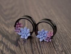 two pairs of earrings with flowers on them sitting on a wooden surface, one is black and the other is blue