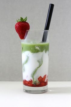 a strawberry and matcha latte in a glass with strawberries on the rim