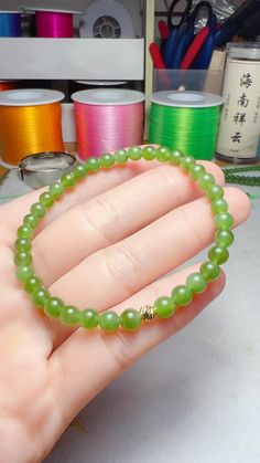 a hand holding a green beaded bracelet in front of some spools of thread