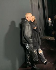 a man and woman standing next to each other in front of a gray wall with black curtains