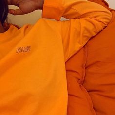 a woman in an orange shirt is holding her hand up to her ear