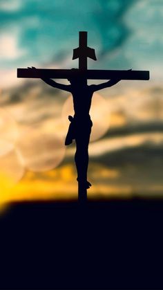 the crucifix is silhouetted against an orange and blue sky with clouds