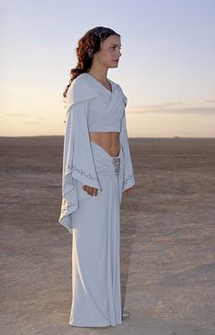 a woman standing in the desert wearing a white dress with cutouts on it's sides