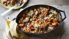 a casserole dish with chicken, tomatoes and spinach in it on a wooden table