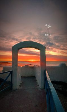 the sun is setting over the ocean with an arch in the foreground that leads out into the water