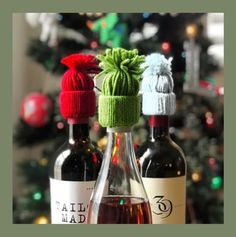 three wine bottles with hats on them sitting in front of a christmas tree, one is empty