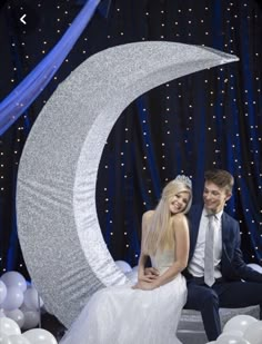 a young man and woman posing for a photo in front of a large crescent moon