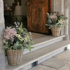 two baskets filled with flowers sitting on the steps next to a wooden door and window