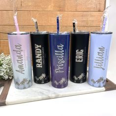 four personalized tumblers with straws in them on a marble tray next to flowers