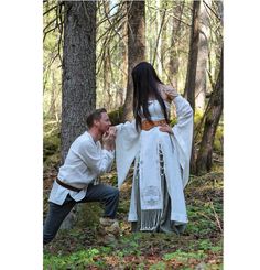 a man kneeling down next to a woman in the woods