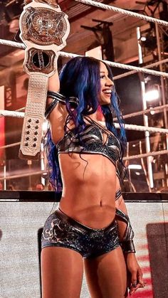 a woman with blue hair and tattoos holding up a wrestling belt in front of a ring