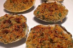 four cooked oysters sitting on top of a white table with seasoning sprinkles