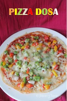 a pizza with vegetables on it sitting on a white plate next to a red table cloth