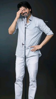 a man standing in front of a microphone with his hands on his face while wearing white pants