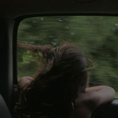 a woman sitting in the back seat of a car with her hair blowing in the wind