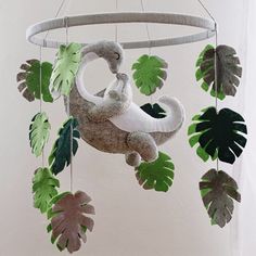 a stuffed animal is hanging from a mobile with green leaves on the sides and an elephant in the middle