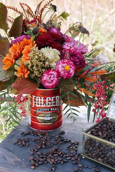 a bouquet of flowers and coffee beans sits on a table next to an old tin can