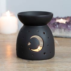 a small black candle holder with a crescent and star design on the top, sitting on a table next to a lit candle