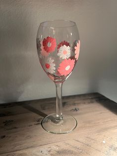 a wine glass with flowers painted on the side sitting on top of a wooden table