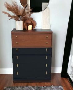 a dresser with a mirror, vase and plants on it in a room that has hardwood floors