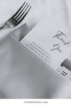 a fork, napkin and thank you note sitting on top of a white table cloth