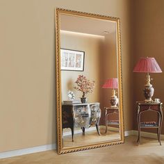 a large mirror sitting on top of a wooden floor next to a lamp and table