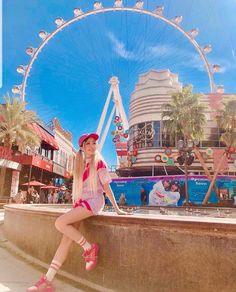 a woman sitting on the edge of a wall next to a ferris wheel