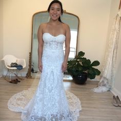 a woman in a white wedding dress standing in front of a mirror and smiling at the camera