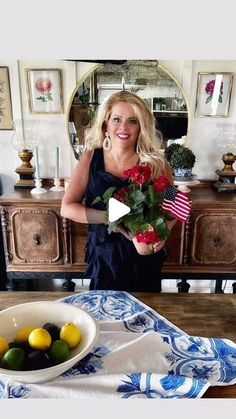 a woman standing in front of a table with flowers and fruit on top of it