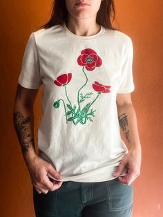 a woman wearing a white t - shirt with red flowers on the front and green leaves on the back