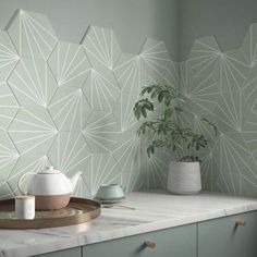 a kitchen counter topped with white vases next to a wall covered in geometric tiles