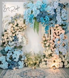 blue and white flowers are arranged on the wall behind a floral arch with candles in front of it