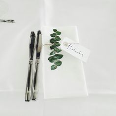 a place setting with silverware, napkins and green leafy leaves on it