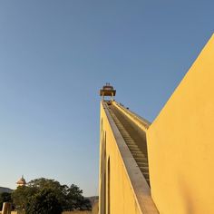 a yellow building with stairs going up to the top and a tower in the background