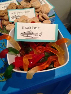 a bowl filled with lots of different colored gummy bears next to a sign that says shark bait