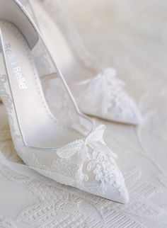 a pair of white high heel shoes sitting on top of a lace covered bed sheet