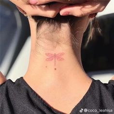 a woman's neck with a small pink dragonfly tattoo on her left side