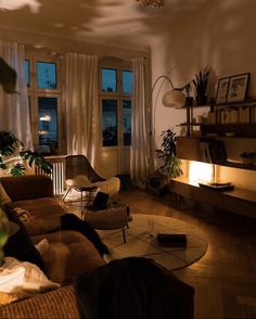 a living room filled with lots of furniture next to tall windows and plants on the wall