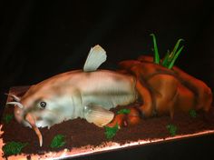 a cake that looks like a fish laying on the ground with seaweed and carrots around it