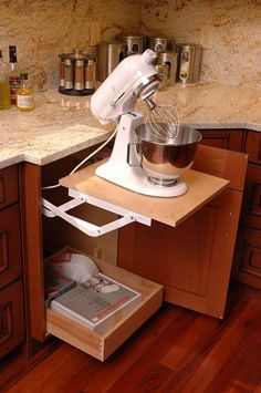 a stand mixer on top of a wooden shelf in a kitchen next to an open drawer