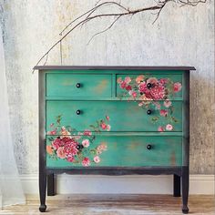 an old dresser with flowers painted on the front and sides, sitting against a wall